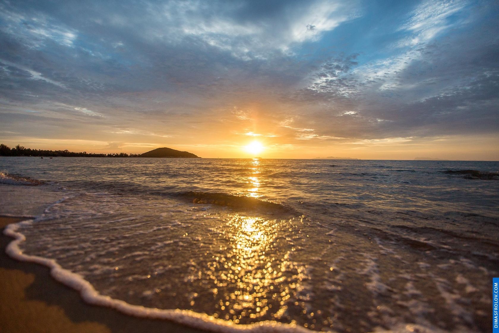 Golden sunset reflecting on a calm beach with gentle waves and a partly cloudy sky