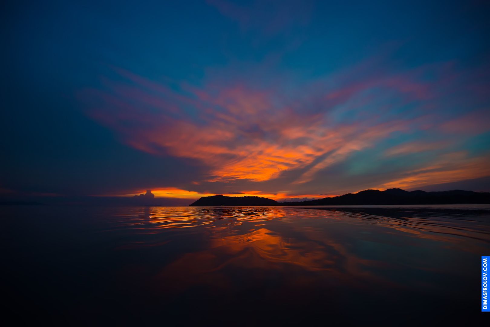 Vibrant sunset over a calm ocean with a silhouette of a small boat on the horizon