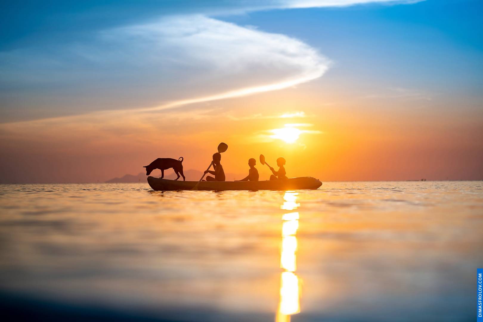 Serene sunset over the ocean with silhouettes of people on a boat, reflecting golden light on the water